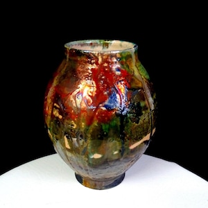 Può includere: Un vaso in ceramica bulboso caratterizzato da uno smalto lucido multicolore con motivi vorticosi di rosso intenso, verde bosco, blu scuro e marrone terra. La superficie presenta una consistenza riflettente simile a gocce.