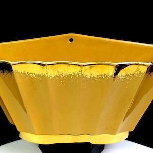 May include: A vintage, yellow, geometric wall pocket planter with a scalloped rim and a hole for hanging. The planter has a gold trim and a textured surface. The planter is made of ceramic.