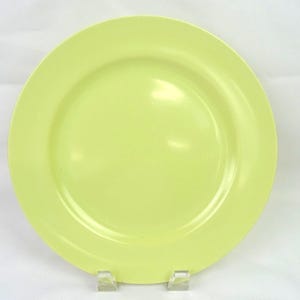 May include: A round, solid light lime green dinner plate with a smooth, glossy finish. The plate features a wide, flat rim and a slightly recessed centre, presenting a clean, minimalist design suitable for various table settings and dining needs.