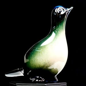 May include: A glass bird figurine featuring a smooth, glossy finish with a color gradient transitioning from deep blue at the head and base to a vibrant emerald green and a creamy white center. The bird has a pointed beak and a small tail.