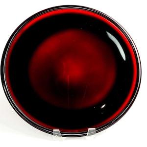 Puede incluir: Un cuenco circular de cristal que presenta un centro rojo intenso que se transforma en un borde negro oscuro. El cuenco tiene una superficie lisa y pulida con un acabado brillante, creando un aspecto reflectante. El diseño es sencillo, redondo y simétrico.