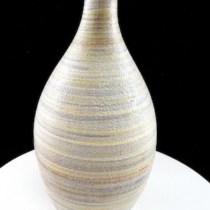 Puede incluir: Un jarrón de cerámica con cuello estrecho y cuerpo redondeado, que presenta una superficie texturizada con bandas horizontales de colores beige apagado, amarillo suave y lavanda pálido. El recipiente tiene un acabado mate y un patrón uniforme.