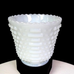 May include: A white milk glass bowl featuring a hobnail pattern across the exterior surface. The bowl has a wide, circular opening with a scalloped rim edge and a tapered base. The glass has a semi-translucent quality with a smooth interior.