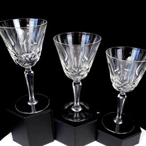 May include: Three clear crystal wine glasses featuring intricate cut glass patterns on the bowls and faceted stems. Each glass stands on a circular base, showcasing a reflective surface and detailed craftsmanship throughout the clear glass structure.