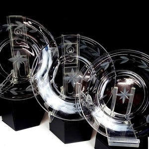 May include: Three clear glass plates with etched leaf and star designs. The plates are displayed on clear stands with black bases, set against a black background. The plates are likely for decorative or serving purposes.