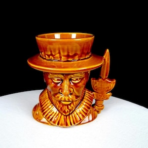 Puede incluir: Taza de cerámica marrón con forma de cabeza de hombre, con sombrero y cuchillo decorativo. La taza tiene una cara detallada con bigote y barba. Probablemente un artículo vintage o antiguo.