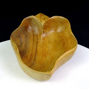 Puede incluir: Un cuenco de madera hecho a mano con una forma orgánica única. El cuenco está hecho de madera de color marrón claro con patrones de vetas visibles. El diseño presenta una estructura en forma de pétalo, creando una pieza visualmente atractiva y funcional.