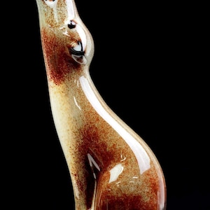 Può includere: Una statuetta in ceramica smaltata e liscia raffigurante un coyote in posizione di ululato, caratterizzata da una tavolozza di colori screziati color crema, marrone chiaro e bruno-rossastro intenso. La scultura ha una finitura lucida.