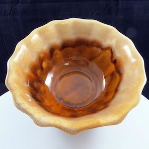 May include: A ceramic bowl with a scalloped edge. The bowl has a colour gradient, going from light tan at the rim to a deep brown in the centre. The interior has a glossy finish, reflecting light. This decorative bowl is suitable for serving.