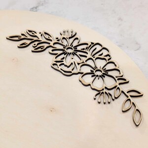 May include: A wooden cutout of a floral design with intricate details. The design features three flowers and leaves, all cut from a single piece of wood.