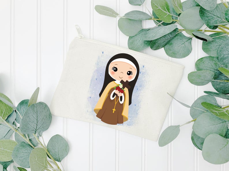 May include: A white canvas zippered pouch with a colorful illustration of a young girl in a brown and white habit holding a cross and flowers. The girl has brown hair and brown eyes. The background is a light blue with white dots.