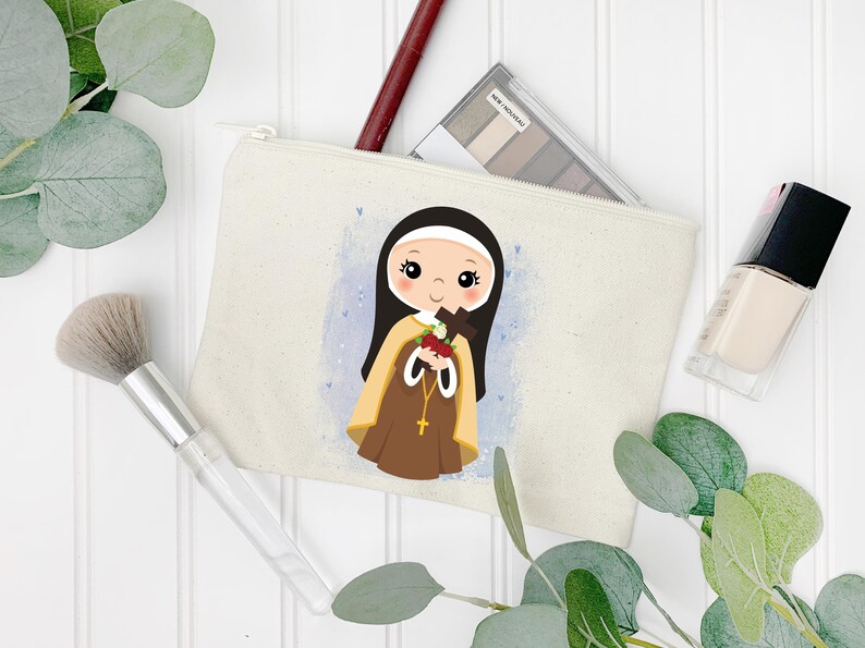 May include: A white canvas makeup bag with a cartoon illustration of a young girl in a brown habit holding a cross and a bouquet of red roses. The girl has brown hair and blue eyes. The background is a light blue watercolor wash with white hearts.
