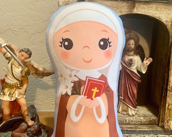 May include: A plush toy of a nun holding a book and flowers. The nun is wearing a brown habit and a white veil. The toy is sitting on a wooden surface.