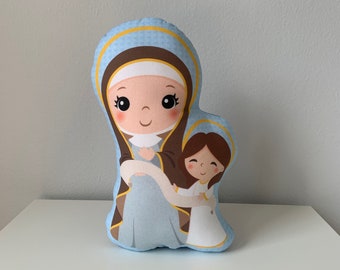 May include: A blue and brown plush pillow featuring a cartoon image of Mary and the baby Jesus. The pillow is a religious themed decoration.