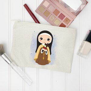 May include: A beige canvas makeup bag with a cartoon illustration of a young girl wearing a brown habit and holding a cross and roses. The girl has brown hair and blue eyes. The background is a light blue watercolor wash.