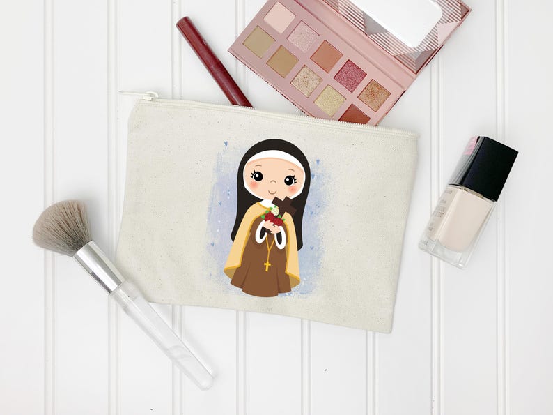 May include: A beige canvas makeup bag with a cartoon illustration of a young girl wearing a brown habit and holding a cross and roses. The girl has brown hair and blue eyes. The background is a light blue watercolor wash.