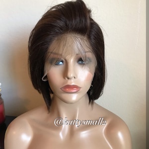 May include: A brown bob wig with a lace front is displayed on a mannequin. The wig has a natural-looking hairline and a short, sleek style. The mannequin's face is visible, with painted features and a neutral expression. The text "@kattysmall2" is visible.