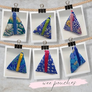 May include: Six triangular zippered pouches with different colourful patterns. The pouches are hanging on a clothesline with clothes pegs. The text "wee pouches" is written below the pouches.