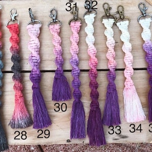 May include: Ten colorful crocheted keychains with tassels. The keychains are ombre, with colors transitioning from pink to purple. The keychains are numbered 27, 28, 29, 30, 31, 32, 33, 34, and 35.