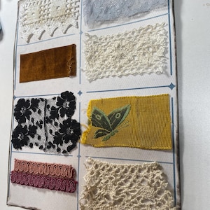 May include: A collection of different lace trims, including white, cream, black, and blue. There is also a piece of brown velvet and a yellow ribbon with a green butterfly embroidery.