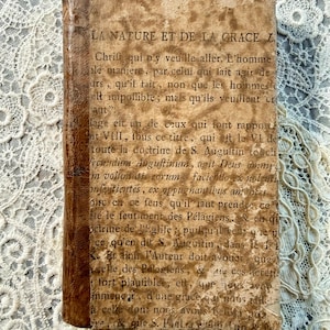 May include: An antique book with a worn, textured cover and spine. The cover features faded text in French, with the title "LA NATURE ET DE LA GRACE Z" visible. The book's pages show signs of age and wear.