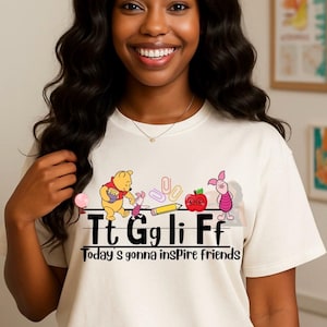 Puede incluir: Camiseta color crema con un gráfico de los personajes de Winnie the Pooh, un lápiz y una manzana. El texto de la camiseta dice "Tt Gg li Ff Today's gonna inspire friends."