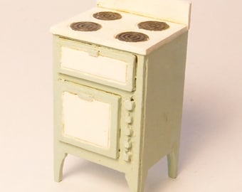 Pode incluir: Um fogão verde e branco em miniatura com quatro elementos de queimador e uma gaveta abaixo do fogão. O fogão tem uma porta de forno branca e uma parte superior branca.