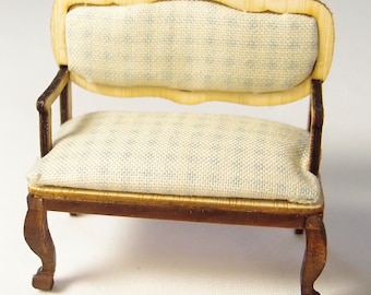 May include: A miniature wooden sofa with a light blue patterned fabric upholstery. The sofa has a curved back and four legs.