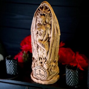 K&ouml;nnte beinhalten: Eine Holzskulptur eines D&auml;mons, der eine Frau in seinen Armen h&auml;lt. Die Skulptur ist mit aufwendigen Details geschnitzt und hat ein Pentagramm am Sockel.