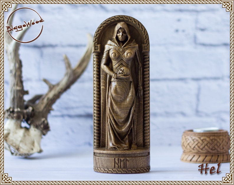 May include: A wooden carving of Hel, the Norse goddess of the underworld, depicted in a hooded robe and holding a skull. The carving is on a wooden base with the inscription "NM".