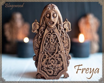 Pode incluir: Uma escultura de madeira da deusa nórdica Freya, com detalhes intrincados e um design tradicional. A escultura é de cor castanho escuro e representa um rosto de mulher com olhos grandes e uma boca larga. A escultura é rodeada por uma borda decorativa de nós e tranças.