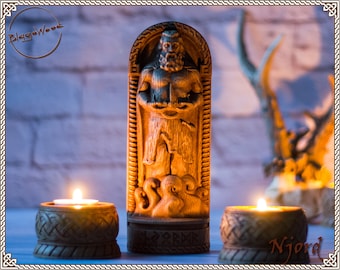 May include: A wooden carving of the Norse god Njord, the god of the sea, standing on a base with runes. The carving is surrounded by two lit candles in wooden candle holders.