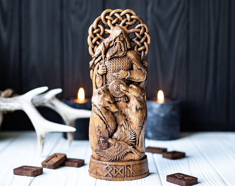 May include: A detailed wooden carving of a seated figure with a beard, holding a staff and shield. The figure is surrounded by animals and a raven. The carving is set against a dark background with candles and wooden runes.