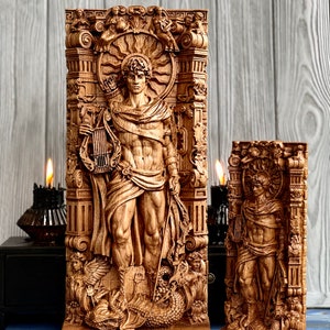 May include: Two wooden carvings of a male figure standing in a decorative frame. The figure is holding a lyre and a staff. The carvings are detailed and intricate, with a sunburst design above the figure's head. The carvings are on a wooden base.