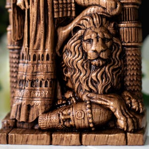 May include: A detailed, brown, carved statue featuring a lion with a flowing mane and a regal pose. The statue has intricate details, including architectural elements and decorative patterns. The lion's paw rests on a cylindrical object.