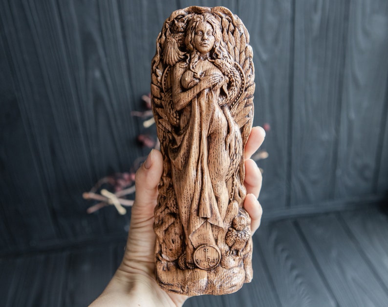 May include: A wooden carving of a woman with long hair and a flowing robe. The carving is detailed and intricate, with a focus on the woman's face and hands. The carving is set against a dark wooden background.