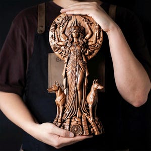May include: A detailed wooden sculpture of a deity with multiple arms, a crown, and flowing robes. Two dog figures flank the central figure. The sculpture is set against a circular backdrop with carved details. The overall design is intricate and detailed.
