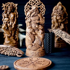 May include: Wooden carvings of Norse gods and symbols. The central figure is a detailed sculpture of a bearded man with bears, a shield, and a bird. Other carvings include a woman with a child, a wolf, and a round wooden piece with a symbol.
