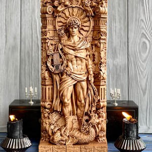 May include: A wooden carving of a male figure with a lyre and bow and arrow. The figure is surrounded by ornate details and a sunburst. The carving is on a wooden base.