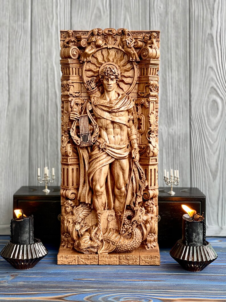 May include: A wooden carving of a male figure with a lyre and bow and arrow. The figure is surrounded by ornate details and a sunburst. The carving is on a wooden base.