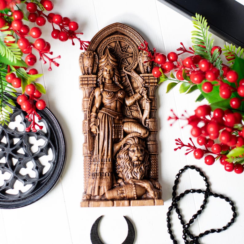 May include: A detailed, brown, carved wooden wall hanging depicting a woman with a bow and arrow, standing on a lion. The artwork features an archway design with owls and a star. Decorative red berries and black accents surround the artwork.