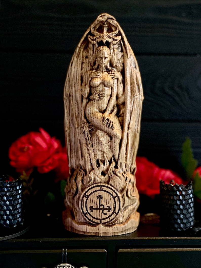 K&ouml;nnte beinhalten: Eine Holzstatue einer Frau mit Fl&uuml;geln und einem D&auml;monenkopf, die auf einem Sockel mit einem Siegel steht. Die Statue ist detailliert geschnitzt und hat eine rustikale Oberfl&auml;che.