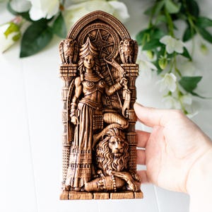 May include: A detailed brown sculpture of a woman with a bow and arrow, seated atop a lion. The sculpture features intricate carvings, including two owls, a star, and architectural elements. The figure is holding a bow and arrow.