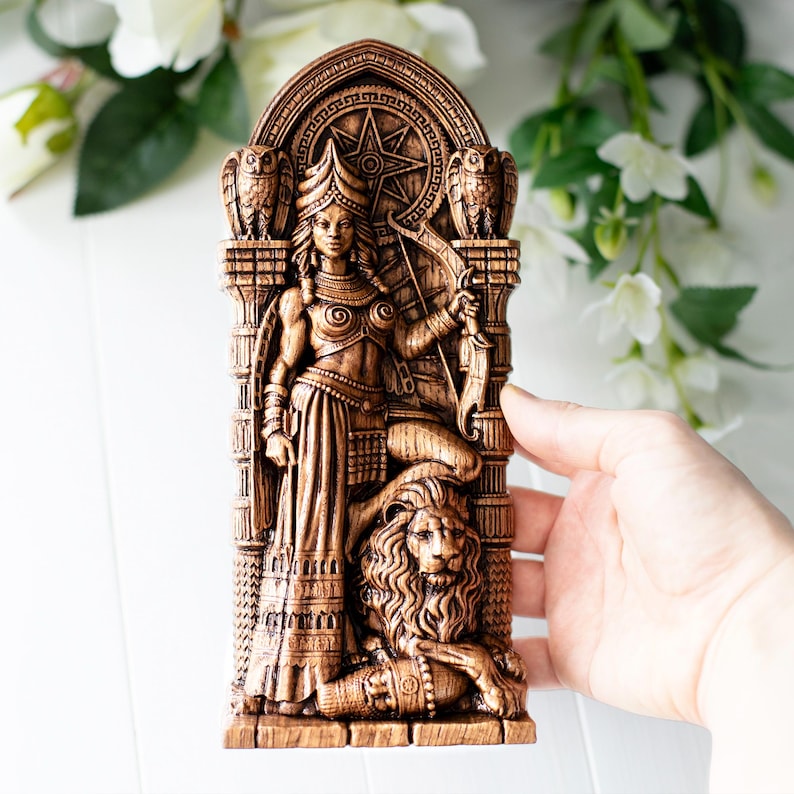May include: A detailed brown sculpture of a woman with a bow and arrow, seated atop a lion. The sculpture features intricate carvings, including two owls, a star, and architectural elements. The figure is holding a bow and arrow.