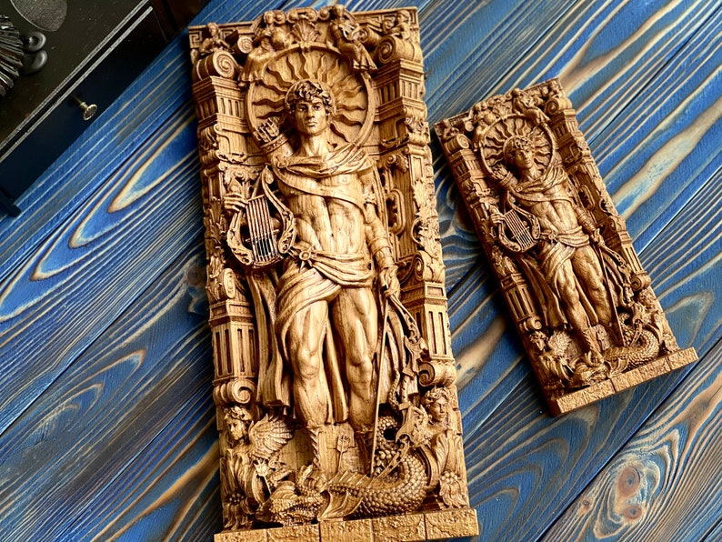 May include: Two wooden wall sculptures depicting a figure holding a lyre. The sculptures are carved in a detailed style and feature intricate designs. The larger sculpture is taller and wider than the smaller one.