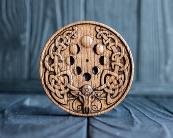 May include: A wooden circular moon phase calendar with a Celtic knot design. The calendar features eight moon phases, a pentagram, and a horned animal head.