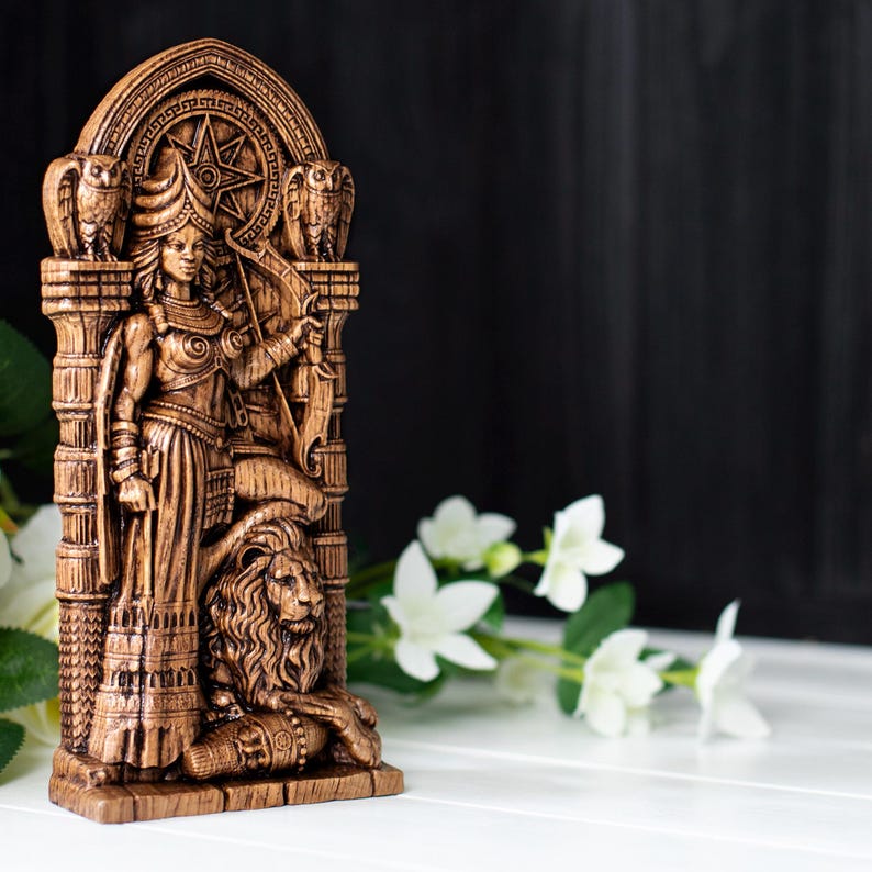 May include: A detailed brown statue depicting a figure with a bow and arrow, flanked by owls, and a lion at the base. The statue has an arched top with a star design. The figure is wearing a long dress and holding a bow.