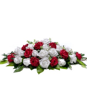 May include: A wedding centerpiece made of white and red roses. The roses are arranged in a long, flowing design. The centerpiece is perfect for a wedding or other special event.