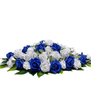 May include: A white and royal blue artificial flower arrangement with roses and greenery. The arrangement is perfect for a wedding or other special event.