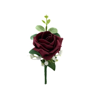 May include: A single burgundy rose with green leaves and white baby's breath, arranged in a boutonniere.